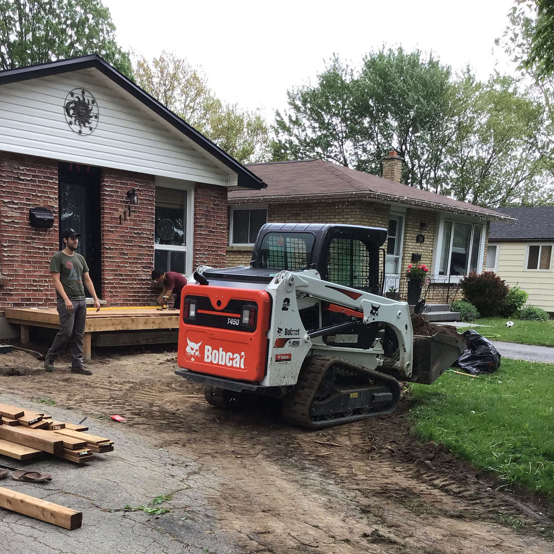 A Bobcat skid steer. A front of a house transformation - landscaping, hardscaping and woodwork project in London Ontario.
